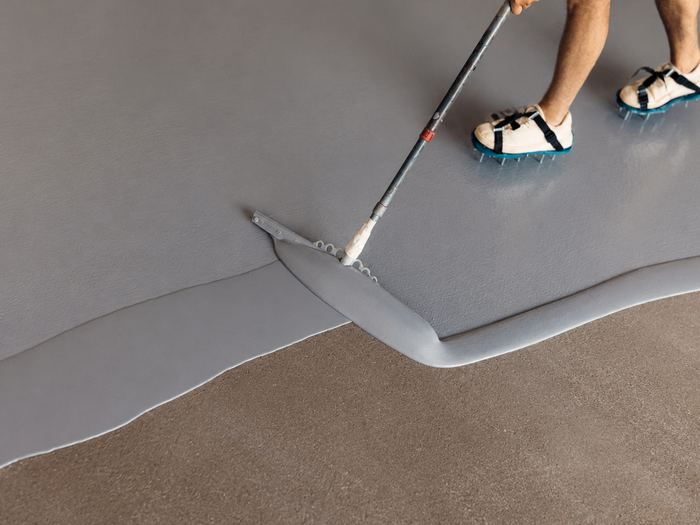 Squeegee spreading grey coating over concrete